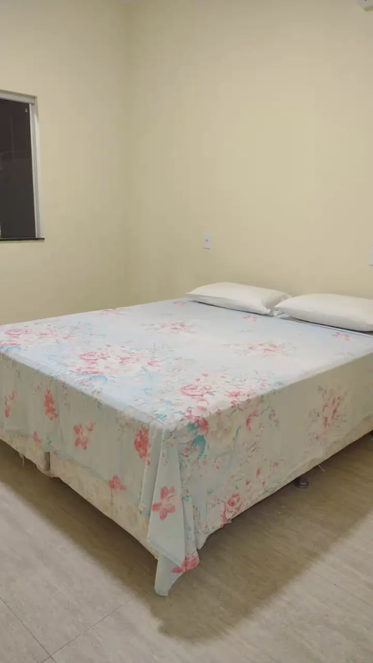 Quarto com cama de casal, roupa de cama floral e janela lateral