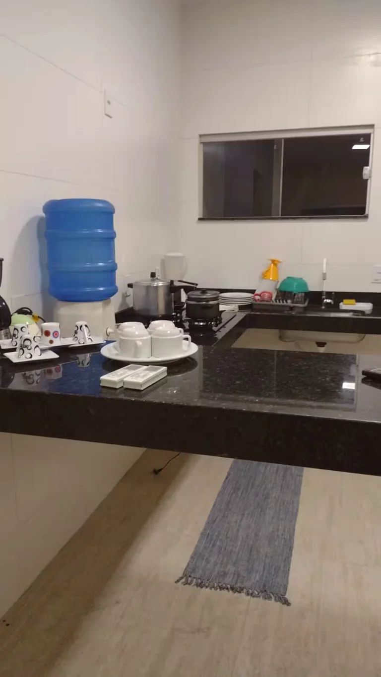 Cozinha com bancada preta, pia, fogao e utensilios sobre a bancada