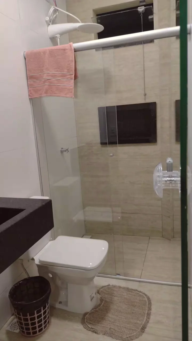 Banheiro com box de vidro, vaso sanitario e bancada preta