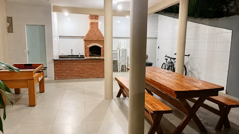 Area coberta com mesa de madeira, churrasqueira de tijolos e mesa de jogos