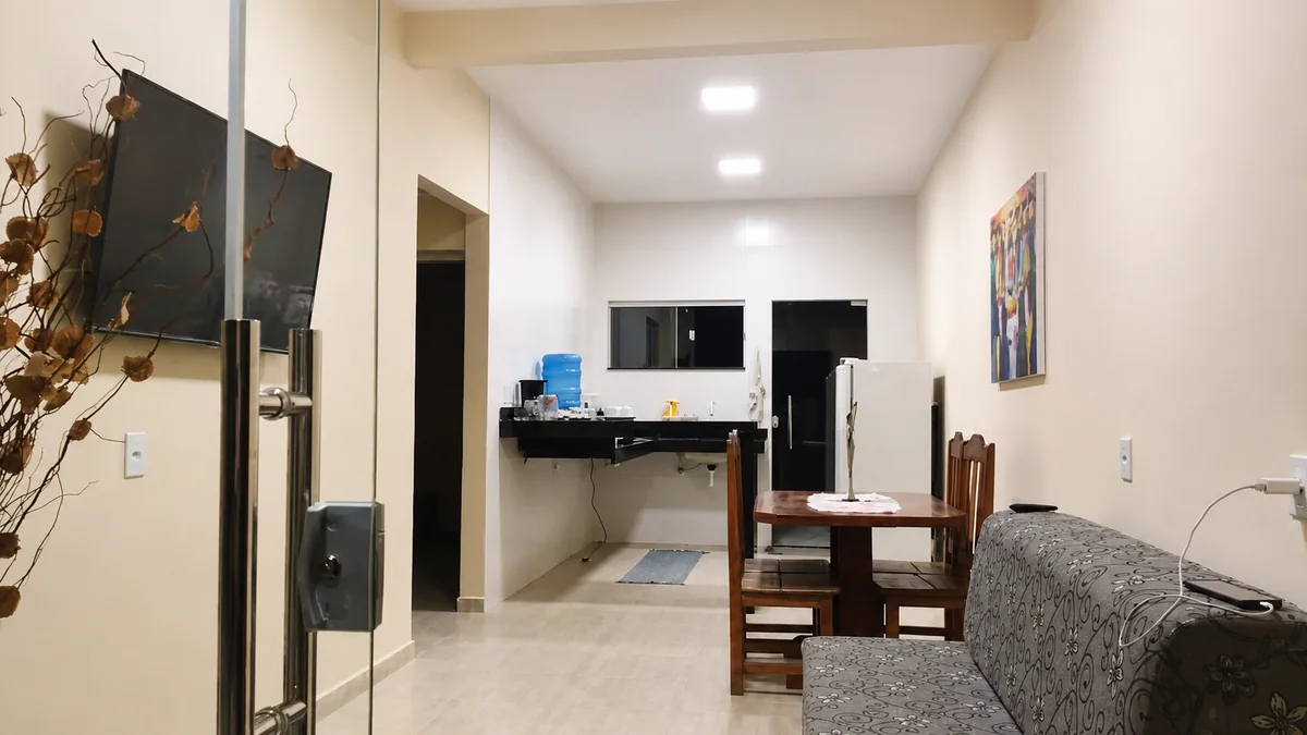 Sala integrada da Casa Capim Santo com sofa, mesa de jantar, TV e cozinha ao fundo