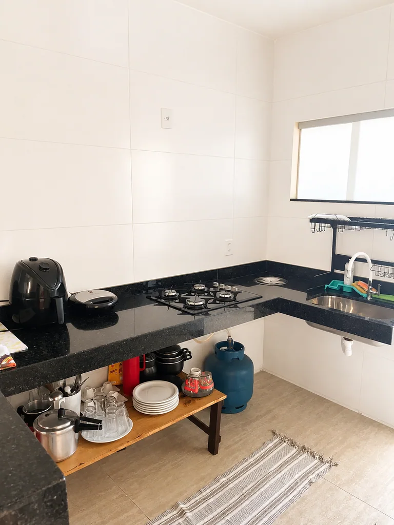 Cozinha com bancada preta, cooktop, pia, pratos e utensilios