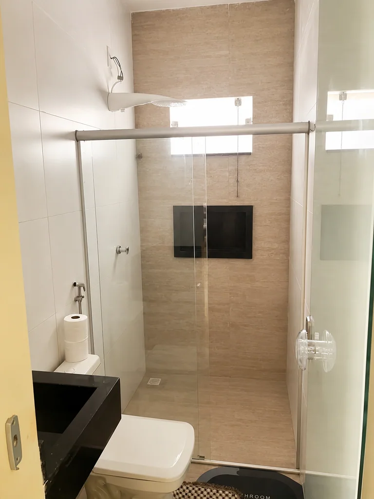 Banheiro com box de vidro, vaso sanitario, bancada preta e espelho redondo
