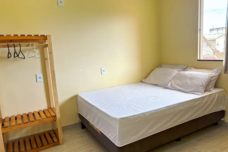 Quarto de casal com cama arrumada arara de madeira e janela com vista