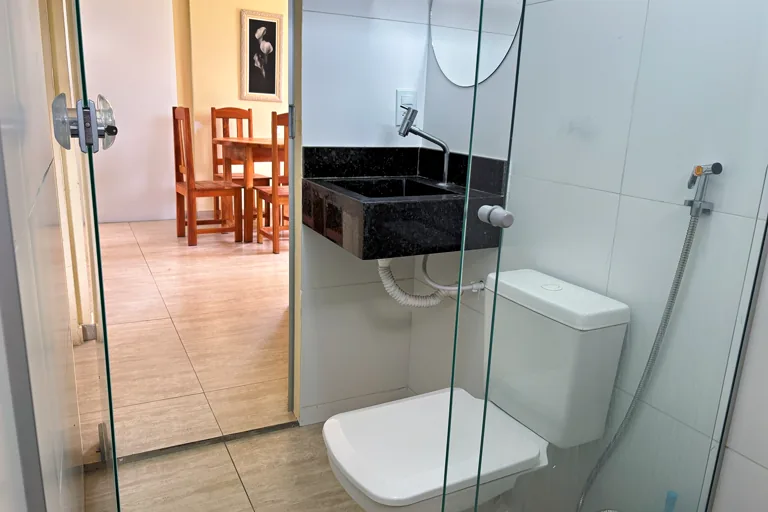 Banheiro social com cuba de granito box de vidro e vista para a sala ao fundo