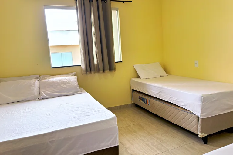 Quarto com cama de casal e solteiro janela com cortina blackout e luz quente
