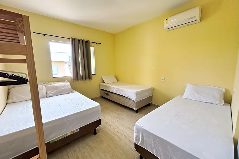 Quarto com cama de casal duas de solteiro ar condicionado e janela iluminada