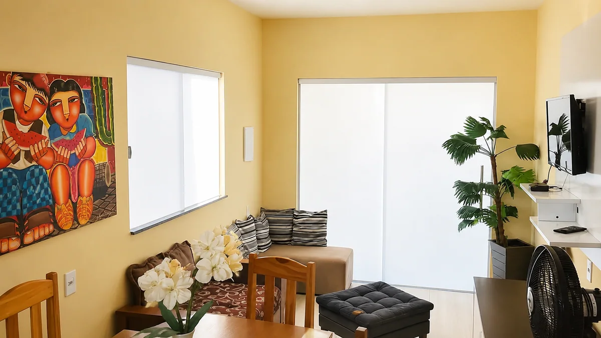 Sala da Casa Eva Doce com sofa, mesa de jantar, TV e planta decorativa