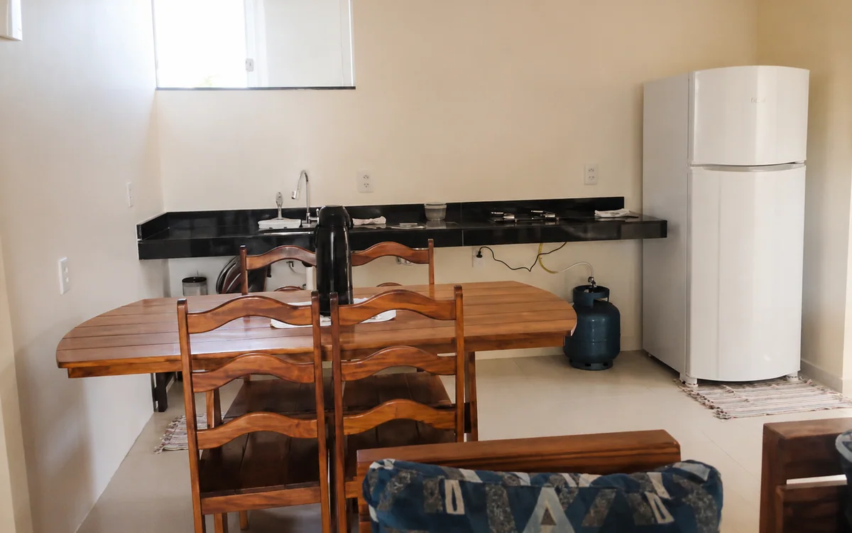 Sala de jantar integrada a cozinha com geladeira, bancada e mesa de madeira