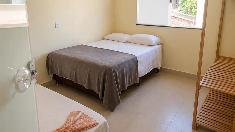 Quarto com cama de casal, cama de solteiro, janela e estante de madeira
