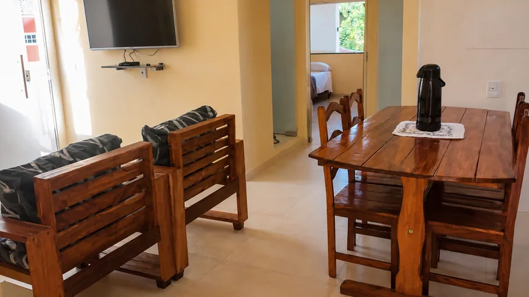 Sala de estar e jantar com sofa de madeira, mesa, TV e acesso aos quartos