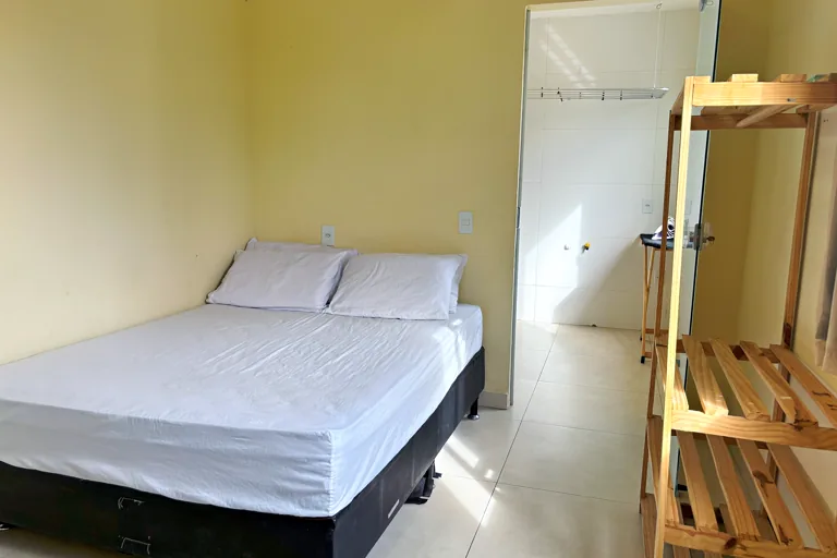 Quarto de casal com lencol branco e acesso a banheiro privativo