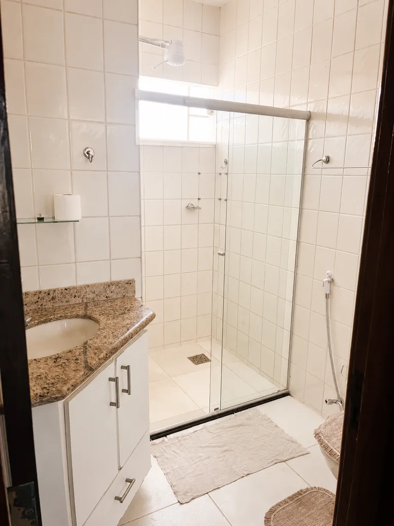 Banheiro com box, vaso sanitario, pia com bancada e espelho