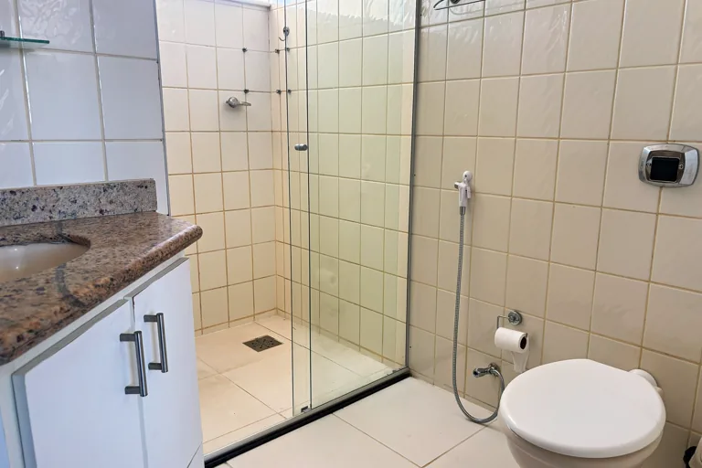 Banheiro com box de vidro vaso sanitario e bancada de granito