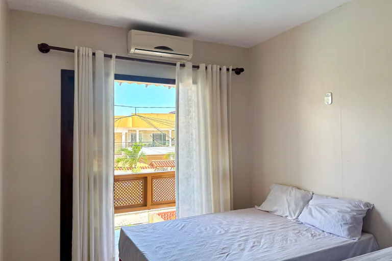Quarto com cama de casal ar condicionado split e janela com vista para a varanda