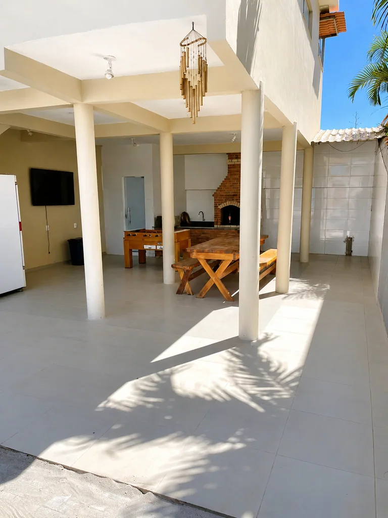 Area externa coberta com mesa de madeira, churrasqueira de tijolos e mesa de jogos