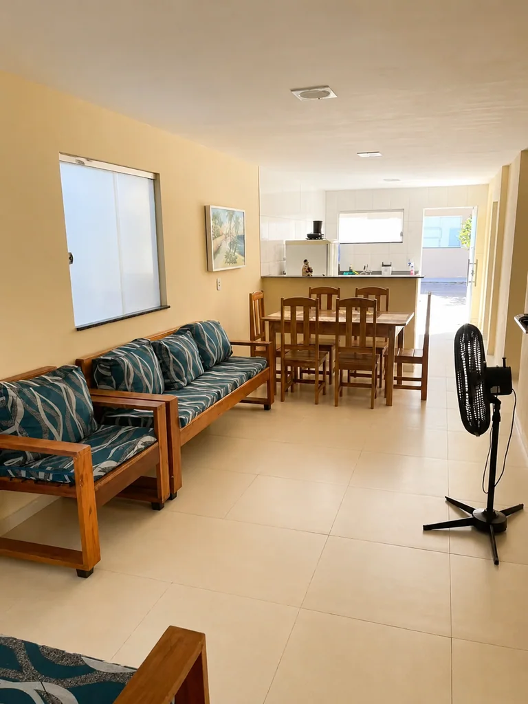 Sala de estar e jantar com sofa, mesa de madeira, ventilador e cozinha ao fundo