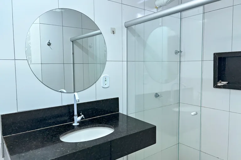 Banheiro com bancada de granito preto, espelho redondo e box de vidro