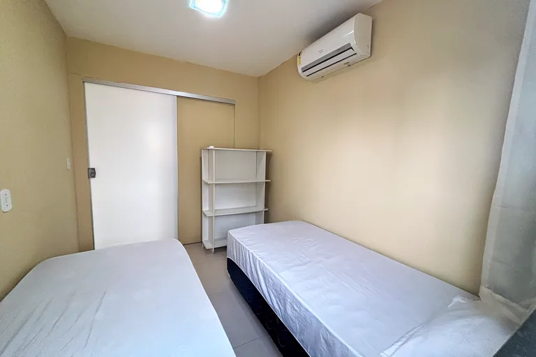 Quarto com duas camas de solteiro, prateleira e ar-condicionado